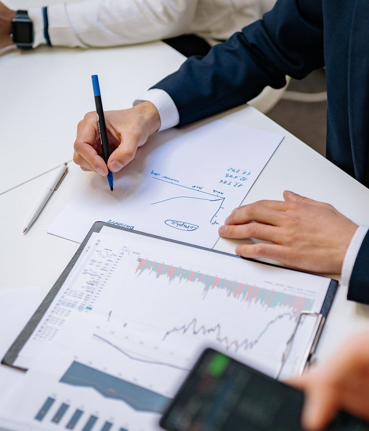 Two people reviewing printed market charts and a hand-drawn growth curve at a desk
